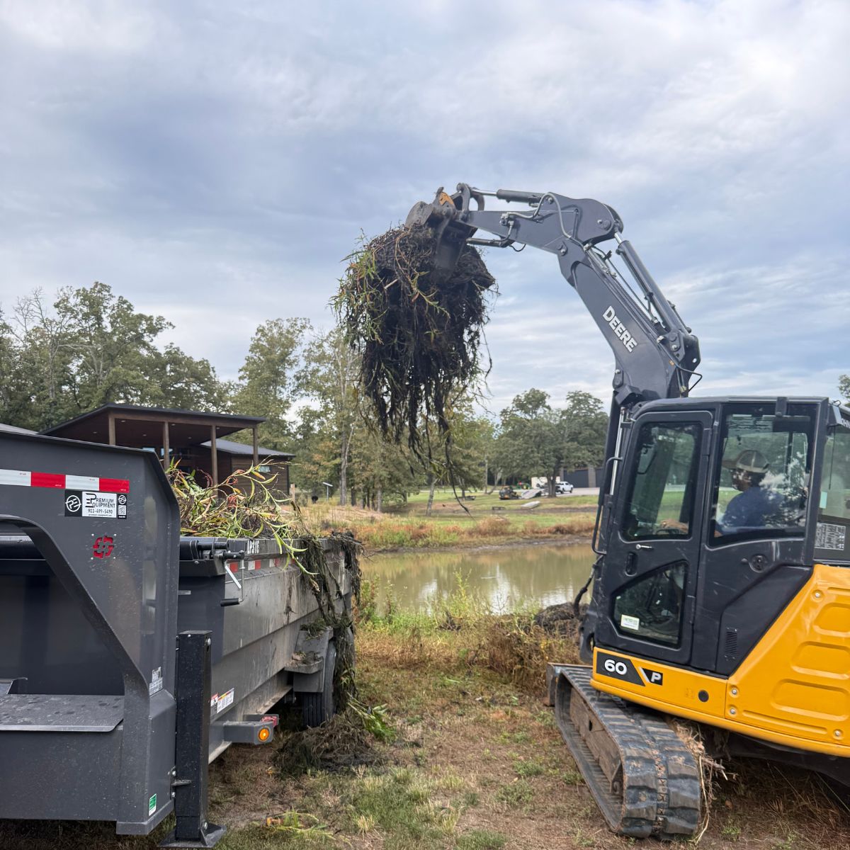 excavator loading dump trailer with moss, cattails from pond cleanout in Paris, Texas